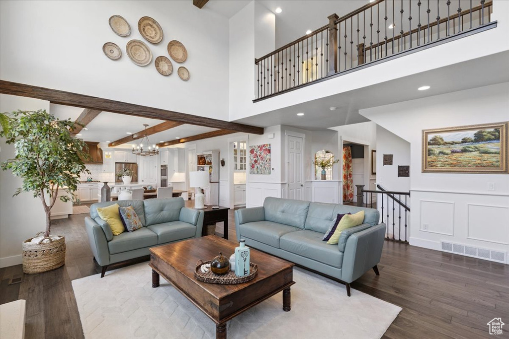 Living area with wood finished floors, a chandelier, a high ceiling, a decorative wall, and beam ceiling