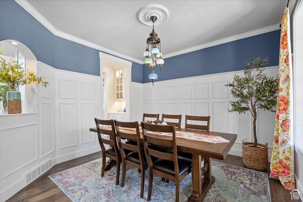 Dining area with a decorative wall, dark wood-style flooring, ornamental molding, wainscoting, and arched walkways