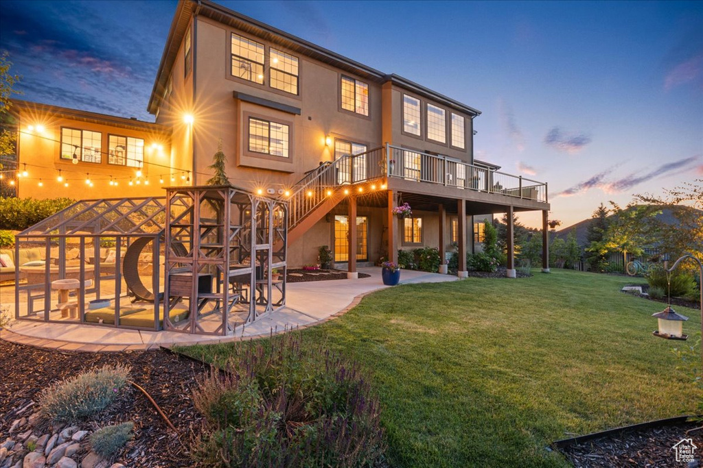 Back of house at dusk with a patio area, stucco siding, a yard, a wooden deck, and stairs