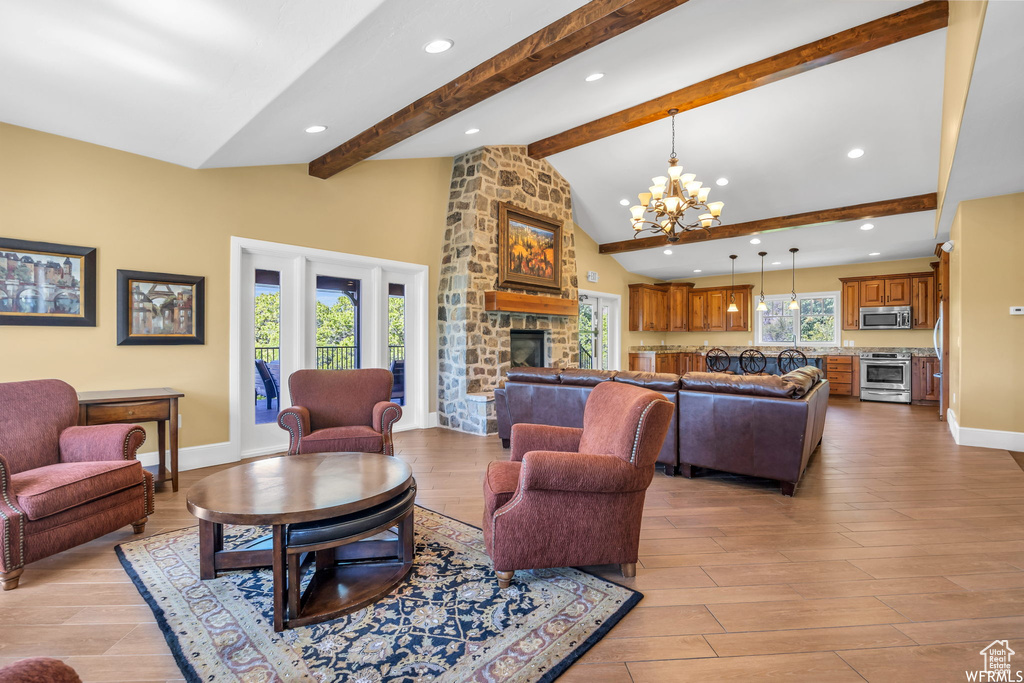 Living area with a stone fireplace, a chandelier, light wood-type flooring, beam ceiling, and recessed lighting