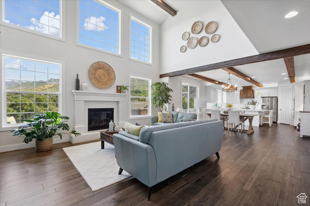 Living area with beam ceiling, dark wood-style flooring, a glass covered fireplace, a chandelier, and recessed lighting