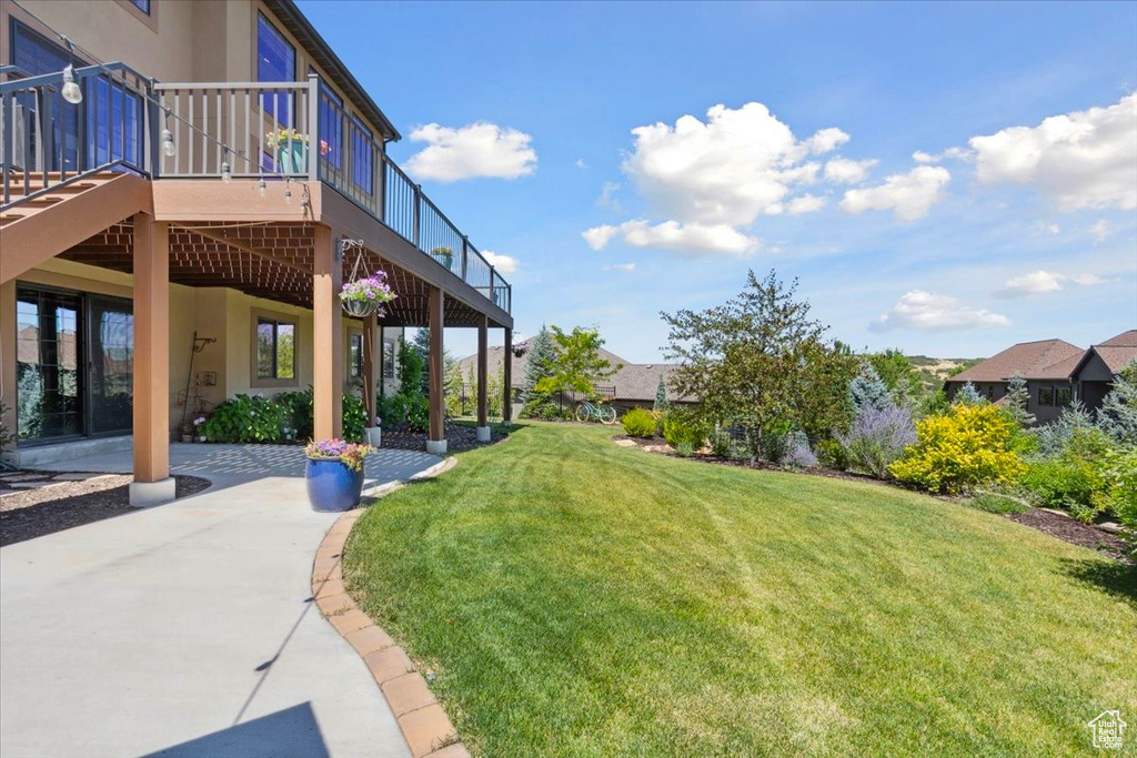View of grassy yard featuring a wooden deck and a patio area