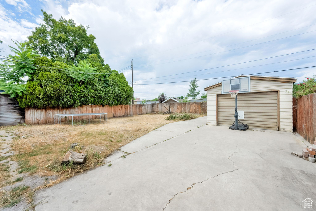 Fenced backyard featuring a trampoline, an outbuilding, and a patio