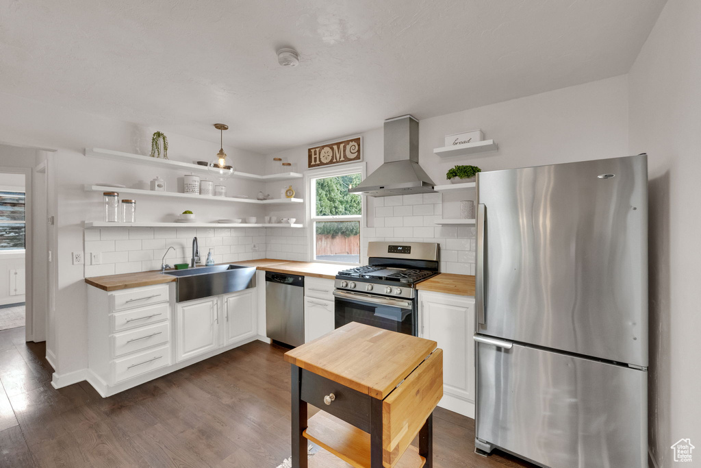 Kitchen with appliances with stainless steel finishes, wall chimney range hood, open shelves, and butcher block counters