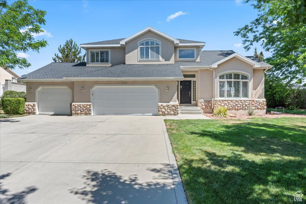 View of front of house with stone siding, stucco siding, driveway, a front yard, and an attached garage