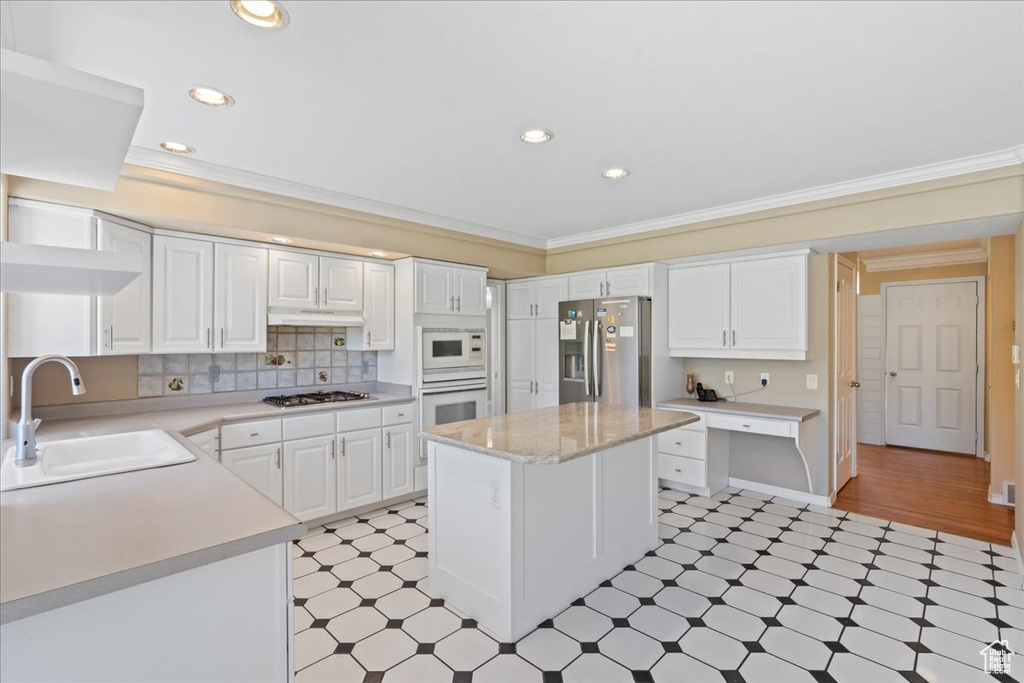 Kitchen featuring stainless steel appliances, light floors, light countertops, ornamental molding, and white cabinetry