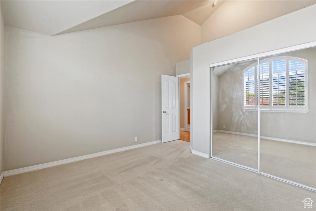 Unfurnished bedroom with vaulted ceiling, light colored carpet, and a closet