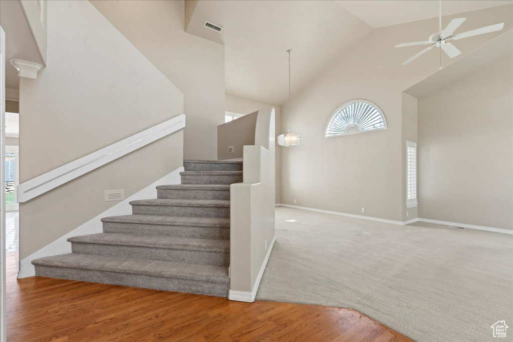 Stairway with high vaulted ceiling, a ceiling fan, and wood finished floors