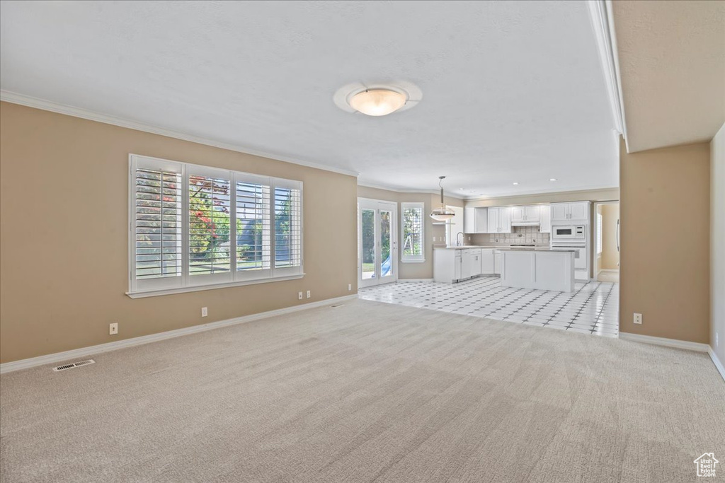 Unfurnished living room with ornamental molding and light colored carpet