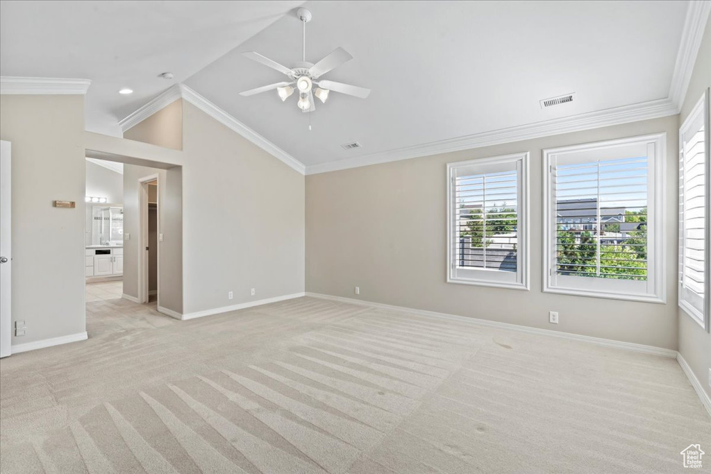 Empty room featuring light carpet, ceiling fan, vaulted ceiling, and ornamental molding