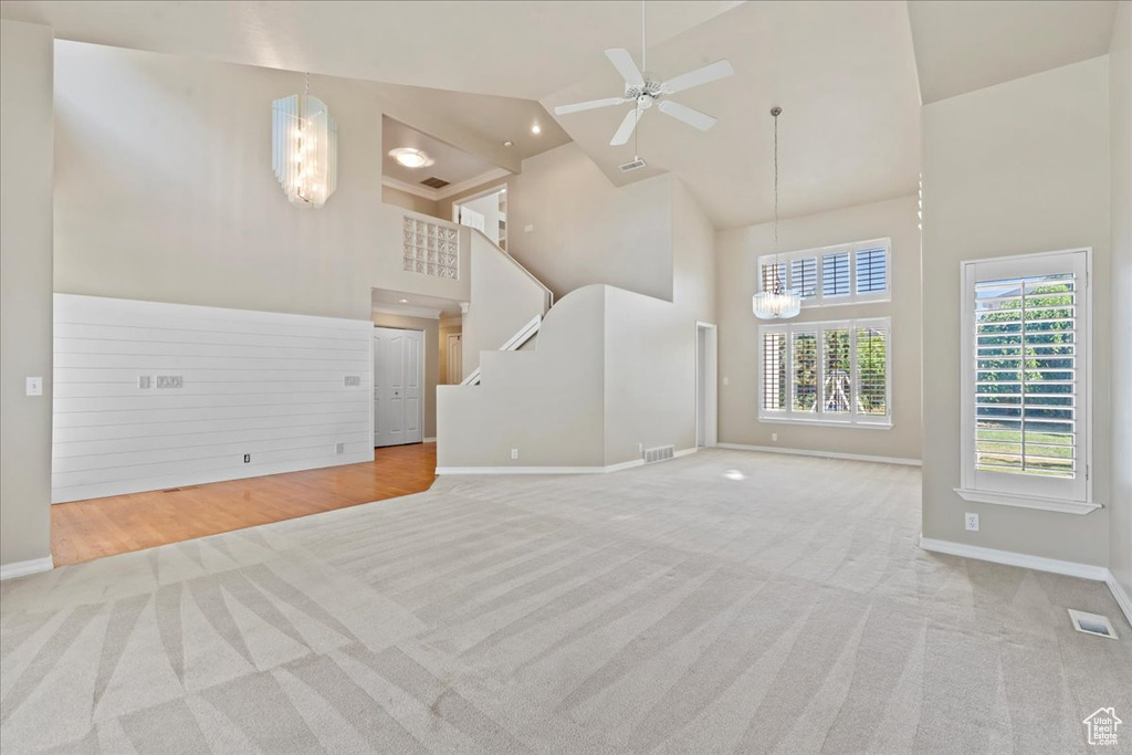 Unfurnished living room featuring a chandelier, high vaulted ceiling, carpet floors, and ceiling fan