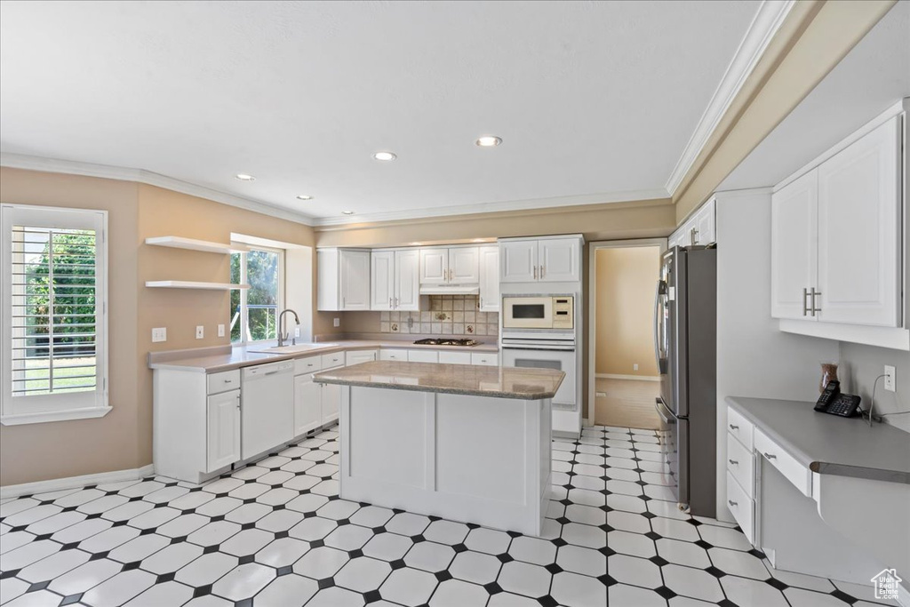 Kitchen featuring white appliances, light floors, a kitchen island, crown molding, and white cabinetry