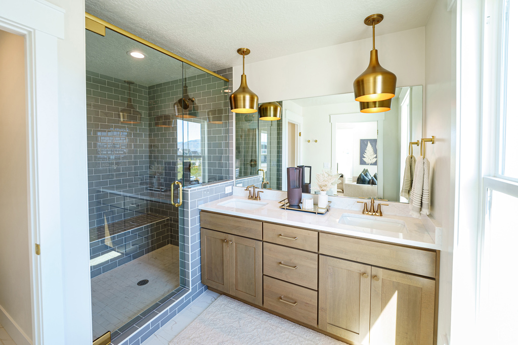 Full bath with double vanity, a shower stall, healthy amount of natural light, a textured ceiling, and recessed lighting