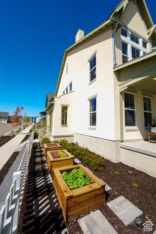 View of side of home featuring stucco siding, a garden, and a chimney