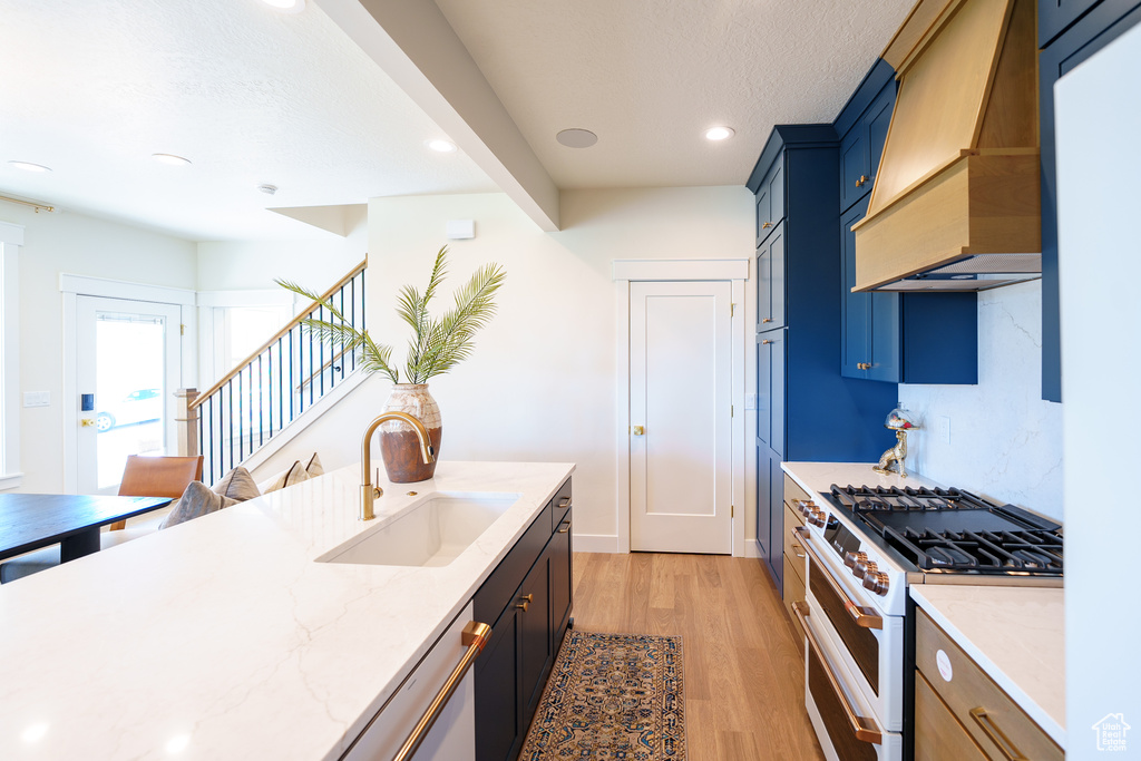 Kitchen featuring white appliances, premium range hood, light wood-style floors, light stone countertops, and recessed lighting
