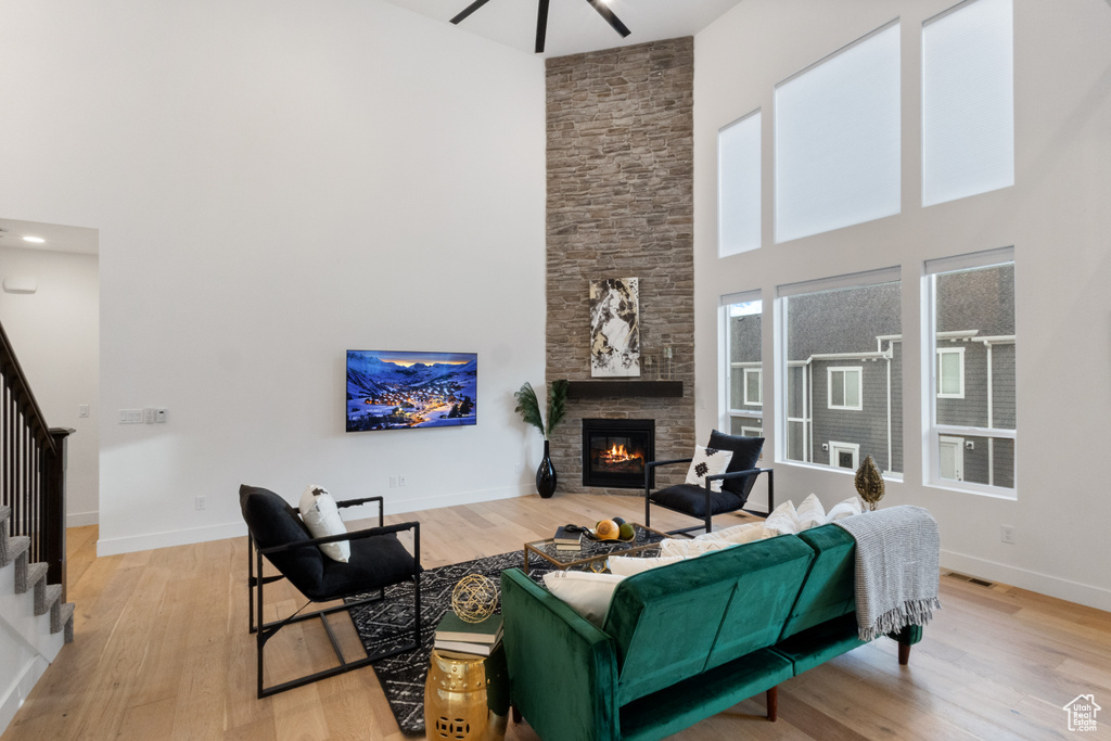 Living room featuring a high ceiling, stairs, light wood-type flooring, a stone fireplace, and a ceiling fan