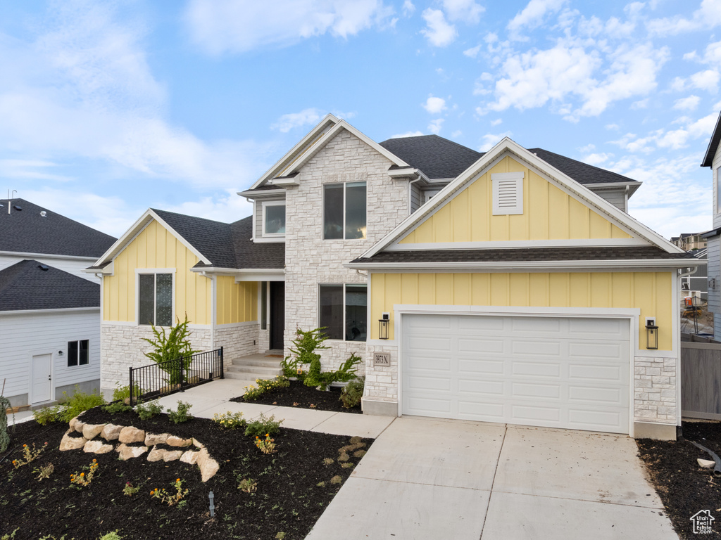 Craftsman-style home with stone siding, board and batten siding, driveway, a shingled roof, and an attached garage