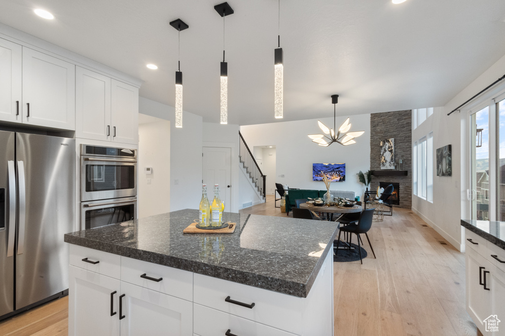 Kitchen with stainless steel appliances, a fireplace, light wood finished floors, a chandelier, and recessed lighting
