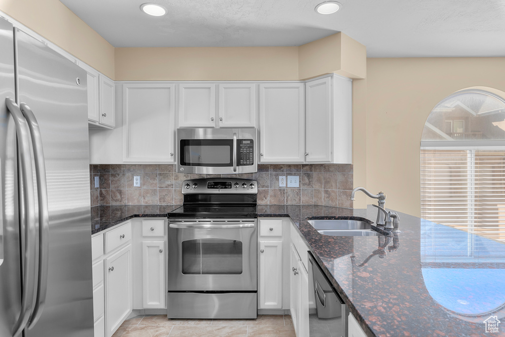 Kitchen with appliances with stainless steel finishes, white cabinetry, dark stone countertops, decorative backsplash, and recessed lighting