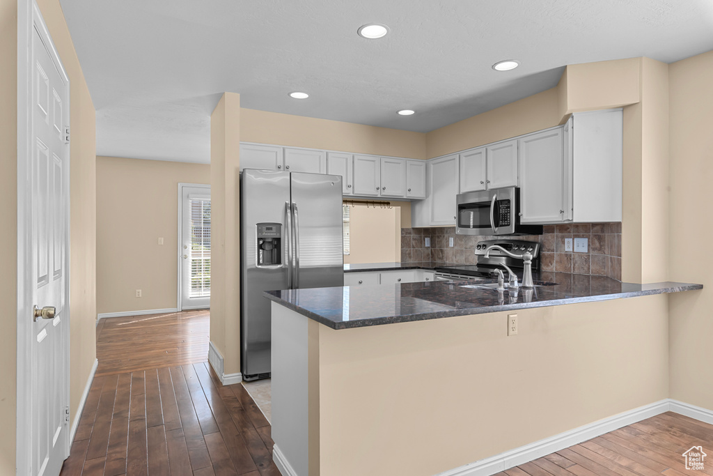 Kitchen with stainless steel appliances, dark stone counters, a peninsula, dark wood-style floors, and backsplash