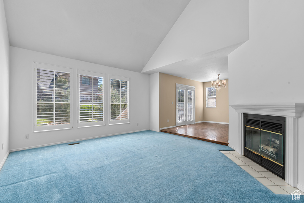 Unfurnished living room with a chandelier, carpet, lofted ceiling, and a fireplace with flush hearth