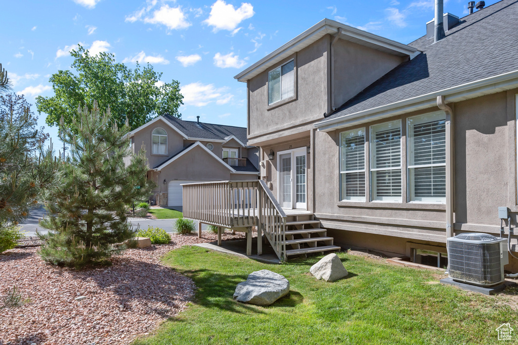 Rear view of property featuring a deck, stucco siding, a lawn, and a shingled roof