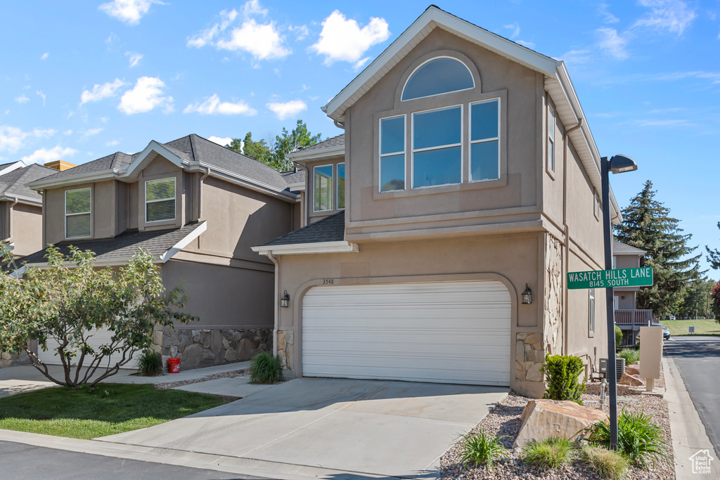 Traditional-style home featuring stucco siding, stone siding, a garage, and concrete driveway