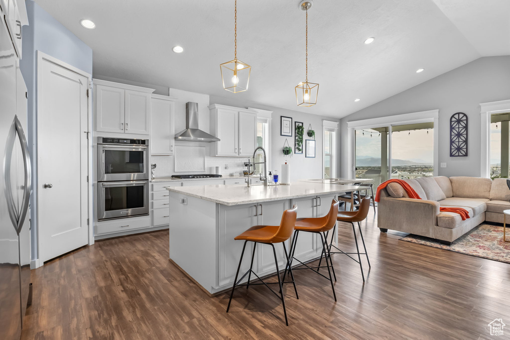 Kitchen featuring wall chimney exhaust hood, stainless steel appliances, lofted ceiling, open floor plan, and dark wood finished floors