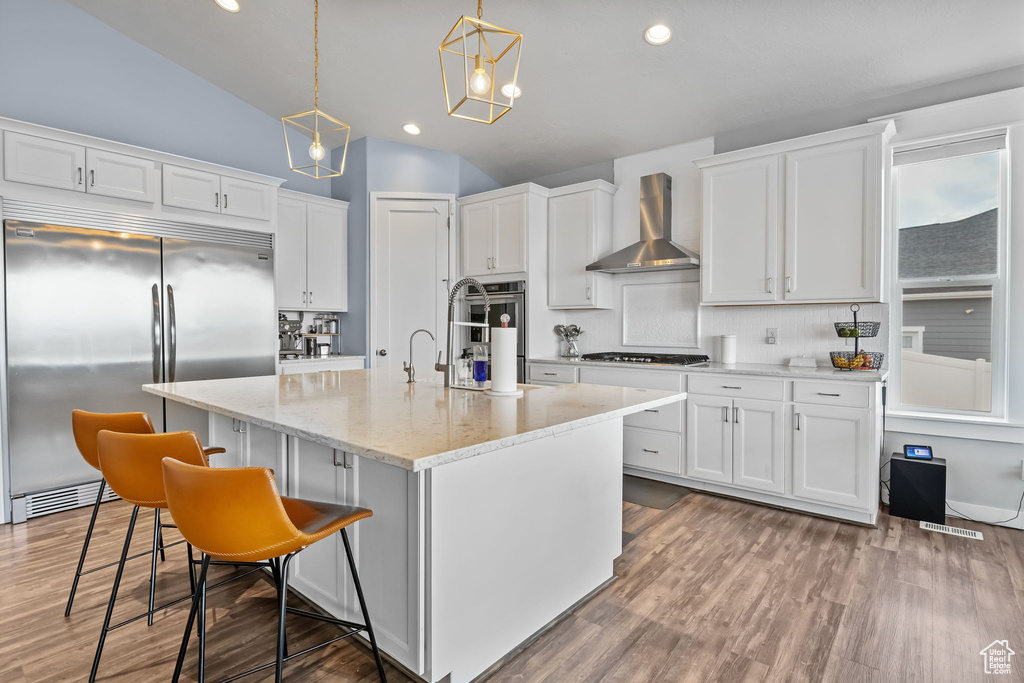 Kitchen with stainless steel appliances, wall chimney exhaust hood, white cabinetry, wood finished floors, and lofted ceiling