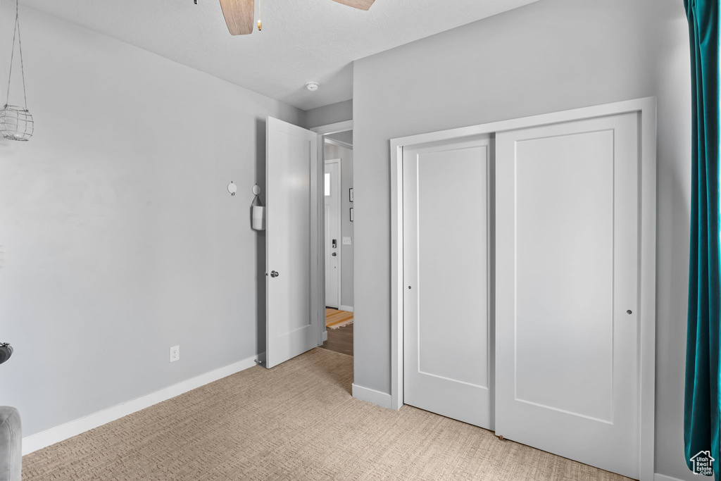 Unfurnished bedroom featuring light colored carpet, a closet, and ceiling fan