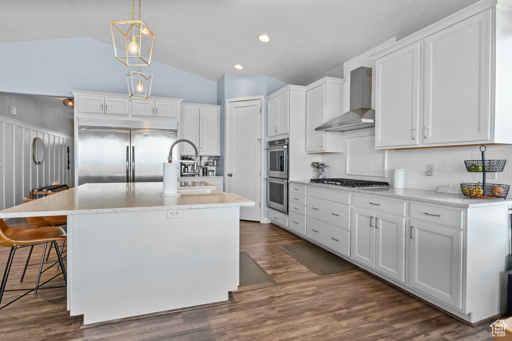 Kitchen with stainless steel appliances, wall chimney exhaust hood, vaulted ceiling, white cabinets, and tasteful backsplash