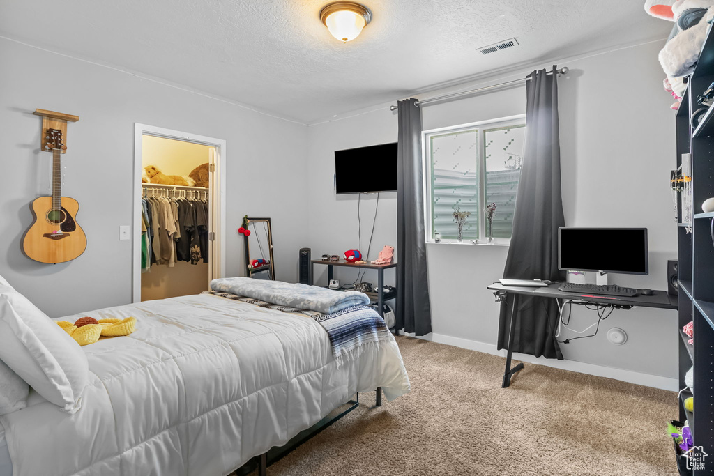 Bedroom featuring carpet, a textured ceiling, and a walk in closet