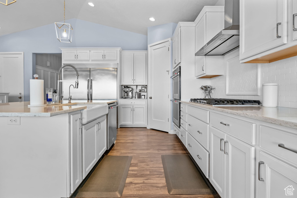 Kitchen with wall chimney exhaust hood, appliances with stainless steel finishes, decorative backsplash, white cabinetry, and lofted ceiling