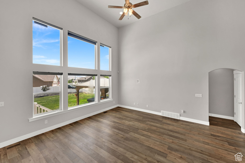 Unfurnished room with arched walkways, a ceiling fan, dark wood-type flooring, and a towering ceiling