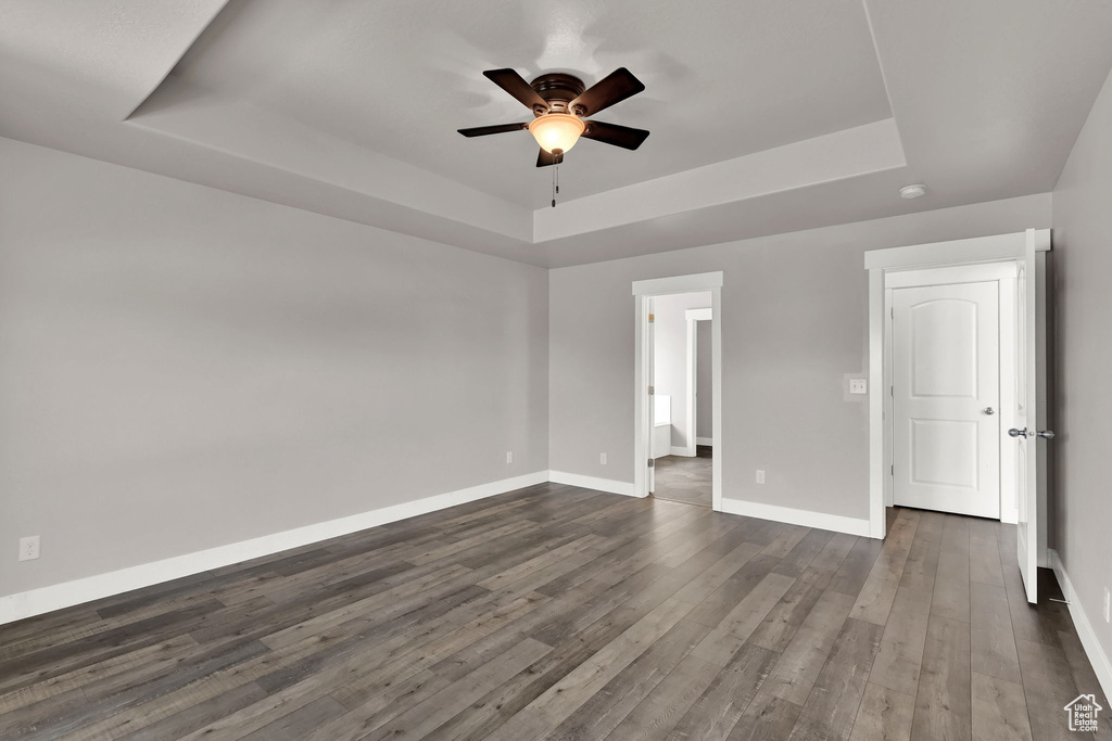 Unfurnished room featuring a tray ceiling, ceiling fan, dark wood-type flooring, and a smoke detector