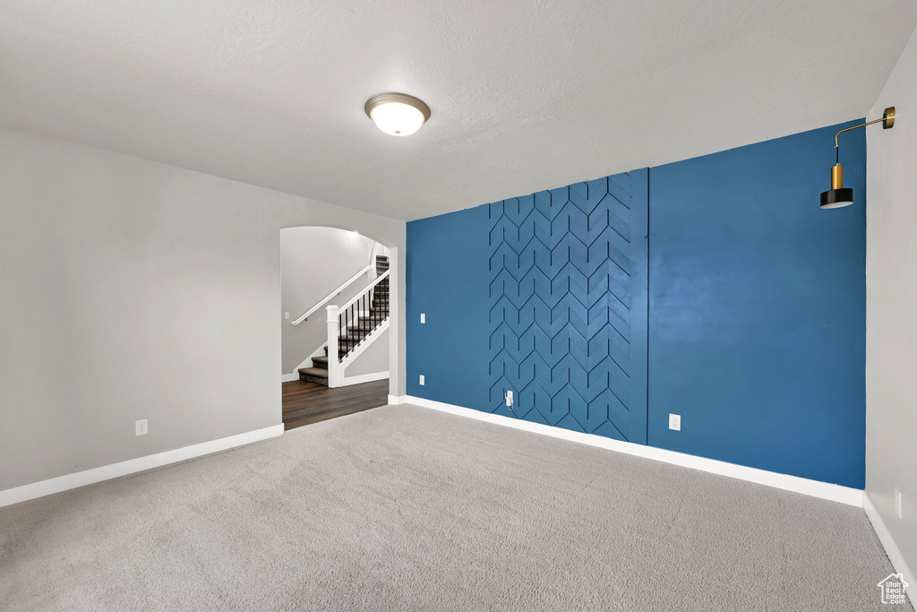 Carpeted empty room featuring arched walkways, stairs, and an accent wall