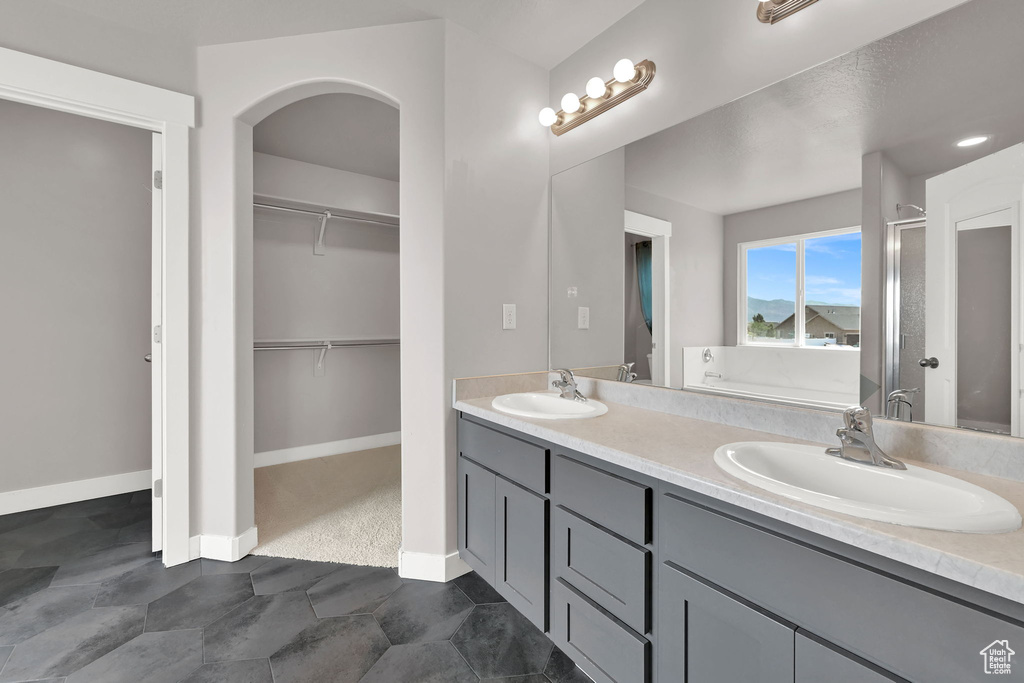 Full bath with double vanity, a spacious closet, a shower stall, and a tub to relax in