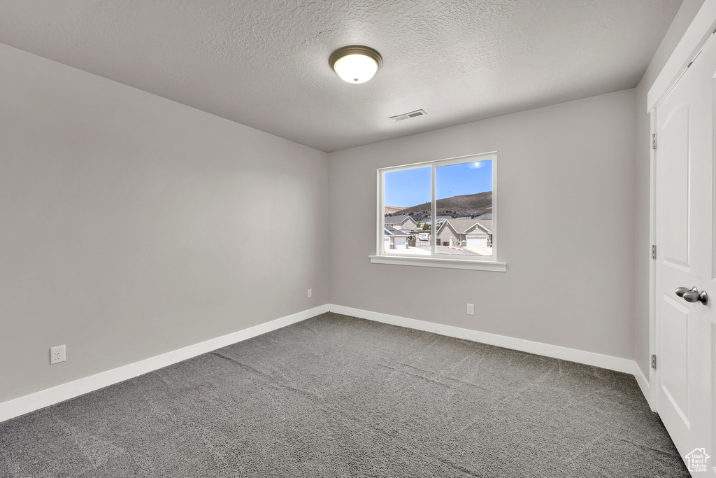 Unfurnished room featuring dark colored carpet and a textured ceiling