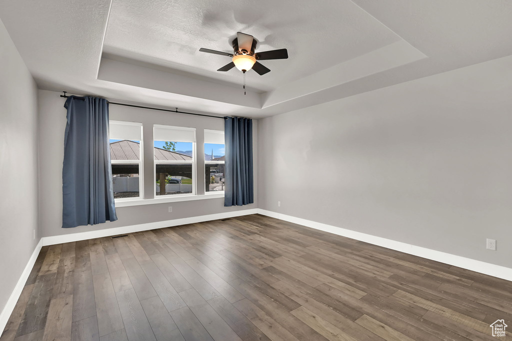 Spare room featuring a tray ceiling, a ceiling fan, and dark wood-style flooring