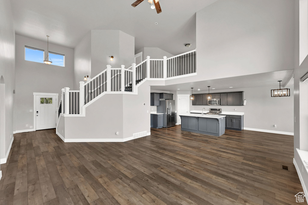 Unfurnished living room featuring a high ceiling, a ceiling fan, dark wood finished floors, and stairs
