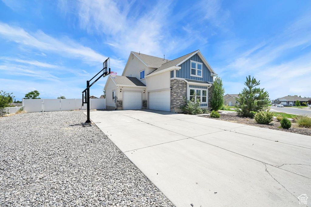 View of front of home featuring board and batten siding, stone siding, concrete driveway, a gate, and a garage