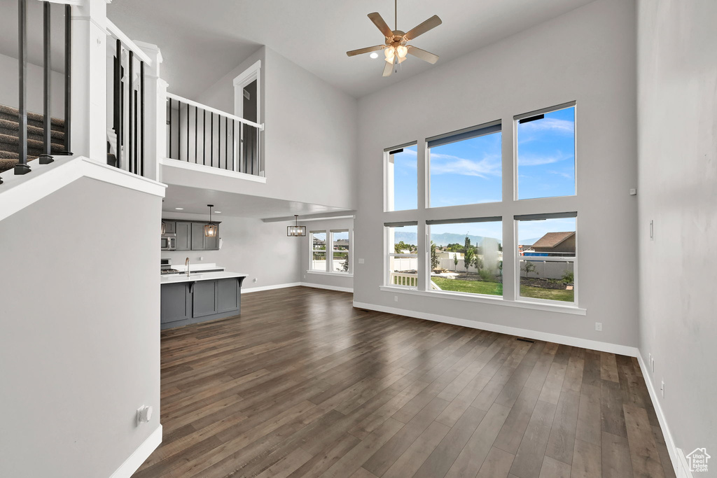 Unfurnished living room featuring a ceiling fan, a towering ceiling, dark wood-style flooring, and stairs