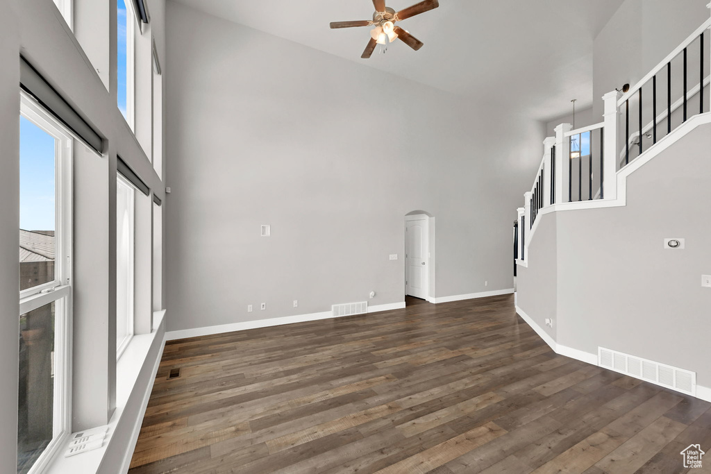 Unfurnished living room with a high ceiling, a ceiling fan, dark wood-style flooring, arched walkways, and stairs