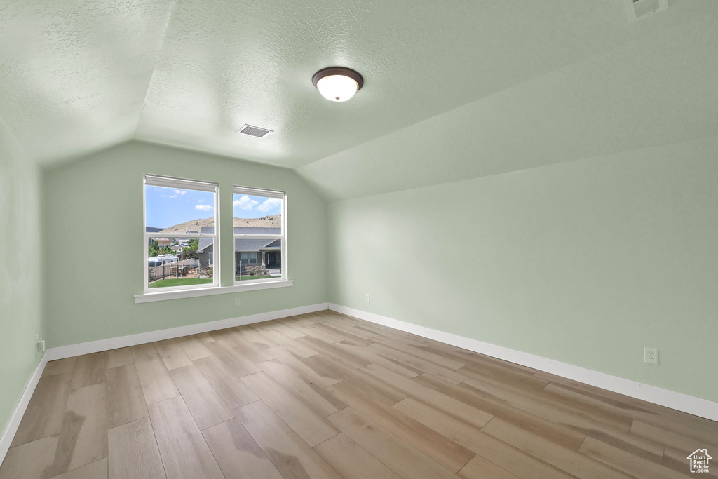 Additional living space with a textured ceiling, wood finished floors, and lofted ceiling