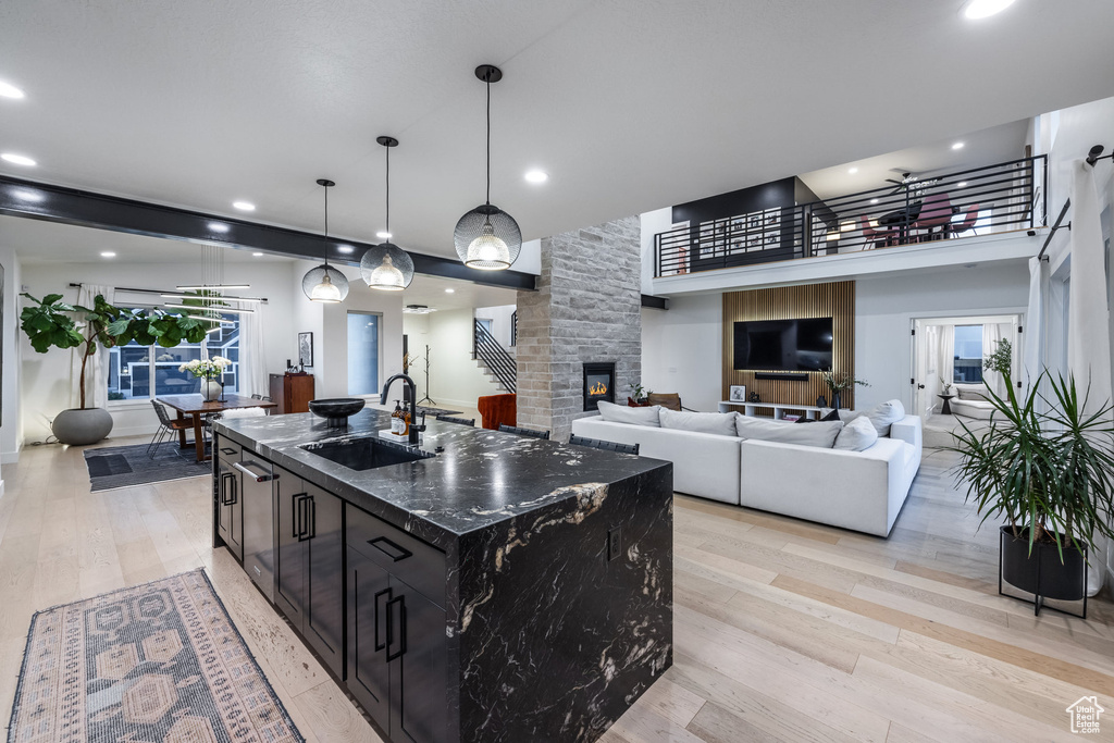 Kitchen featuring a kitchen island with sink, dark cabinetry, light wood-type flooring, dark stone countertops, and a fireplace