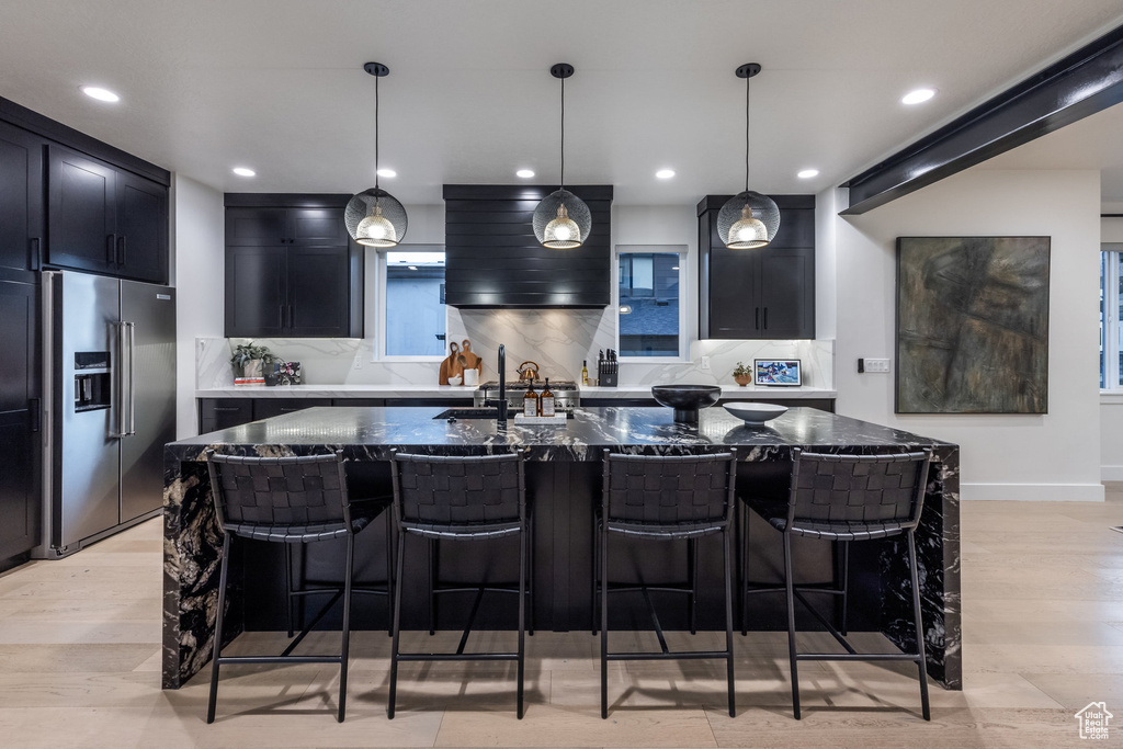 Kitchen with high end refrigerator, dark stone counters, tasteful backsplash, a kitchen breakfast bar, and recessed lighting