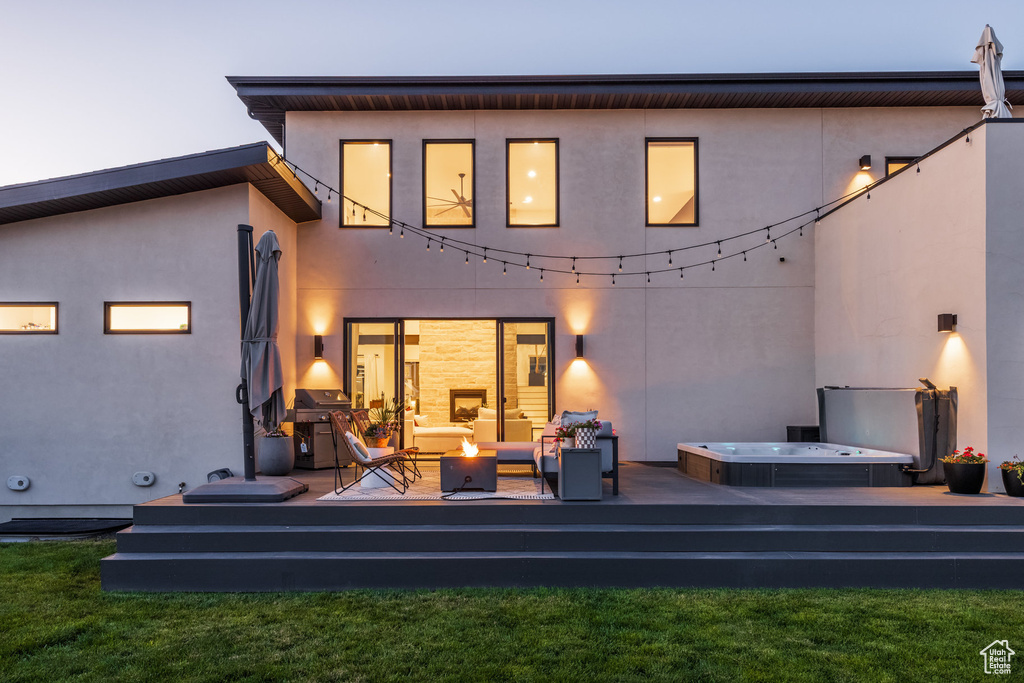 Rear view of house with a covered hot tub, a deck, stucco siding, and an outdoor fire pit