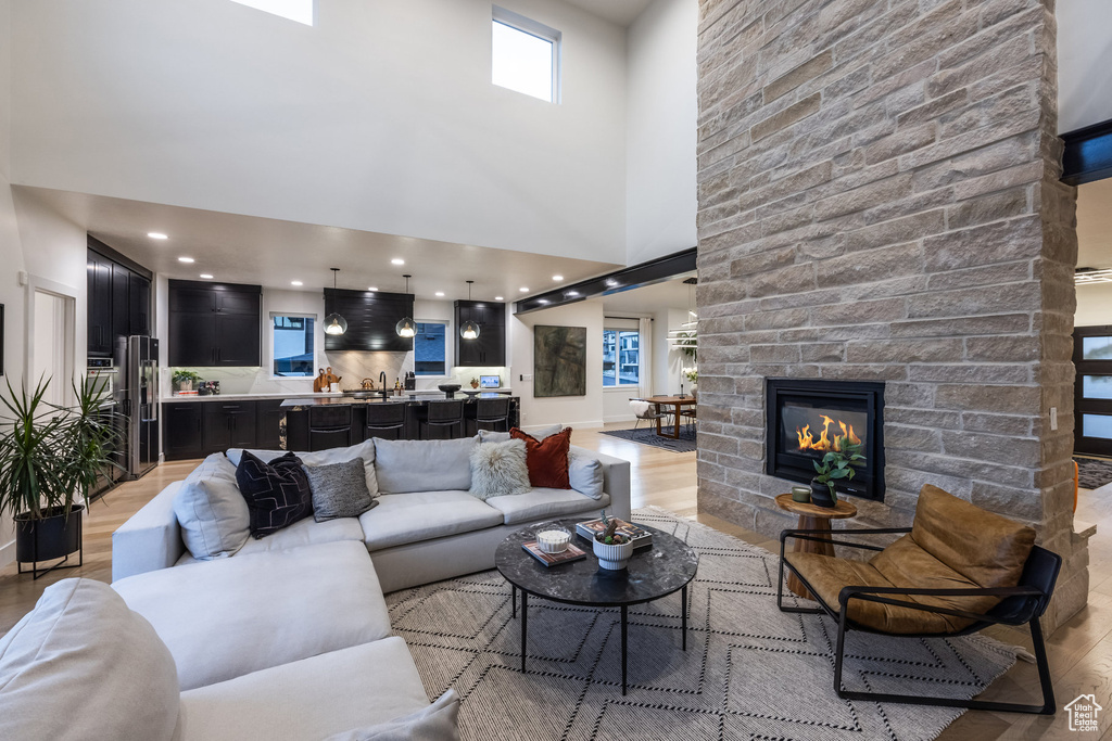 Living room featuring light wood-style flooring, a stone fireplace, and a high ceiling