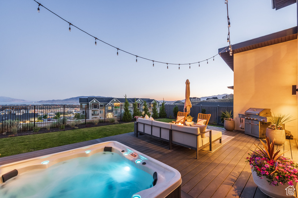 Pool at dusk with a deck, an outdoor hot tub, a fenced backyard, and area for grilling