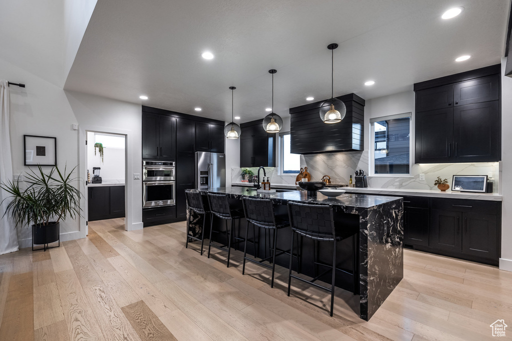 Kitchen with dark cabinets, stainless steel appliances, a kitchen bar, backsplash, and recessed lighting